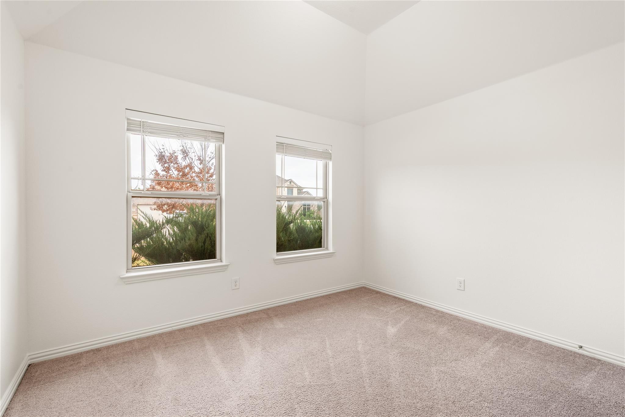 Empty carpeted room with two windows and autumn foliage outside.
