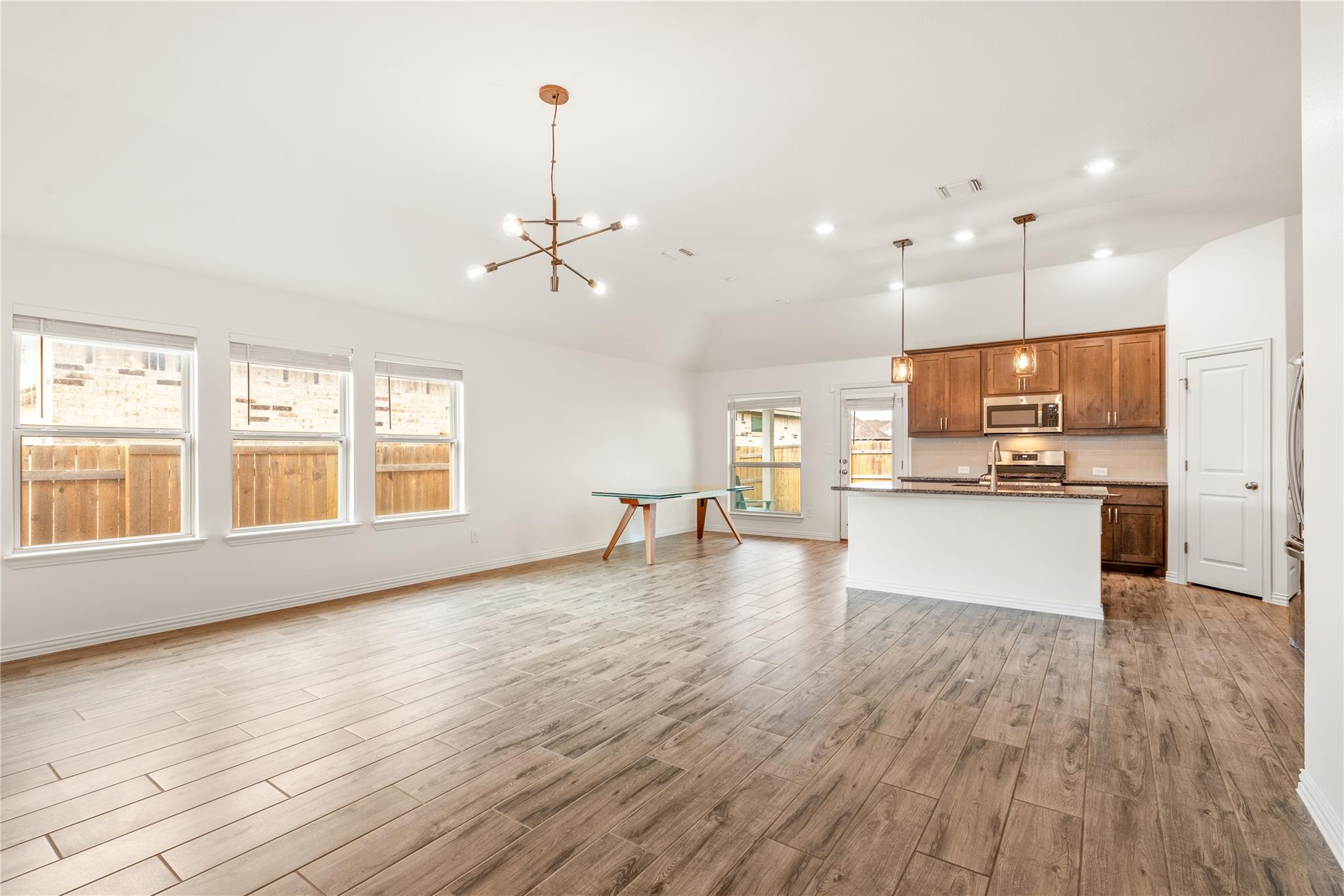 Open-plan living area and kitchen with wood-look tile floors, warm wood cabinets, and a white island.