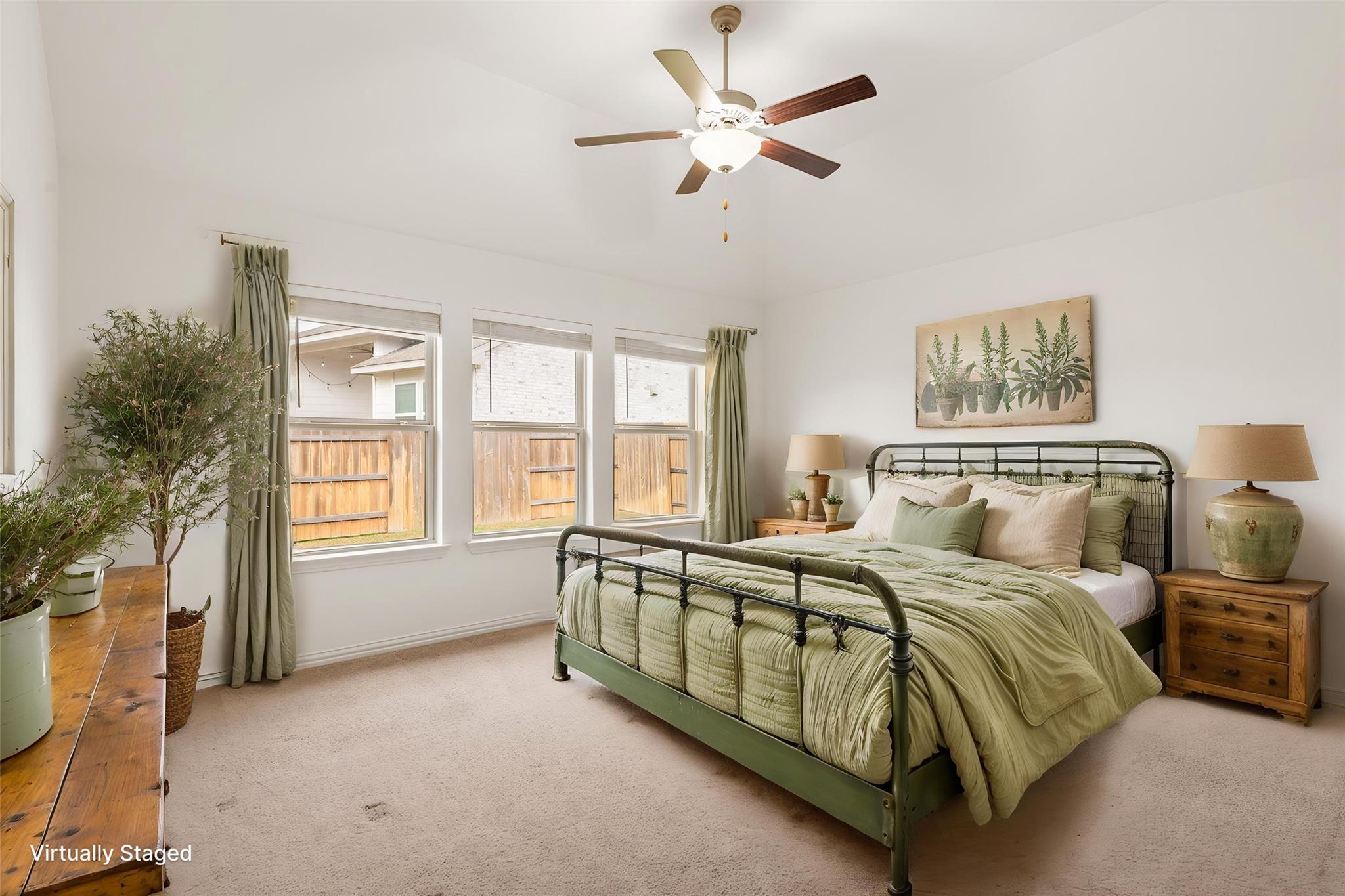 Virtually staged bedroom with green bedding, a metal bed frame, three windows, and potted plants.