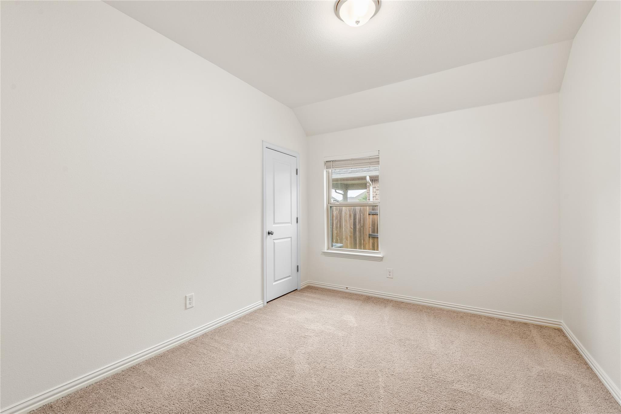 Empty carpeted bedroom with a window and closed white door.