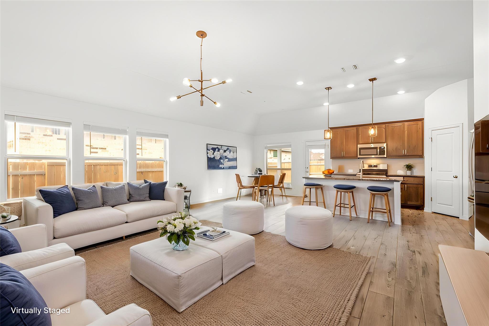 Virtually staged open-plan living room and kitchen with white sofas, wood cabinetry, and a breakfast island.