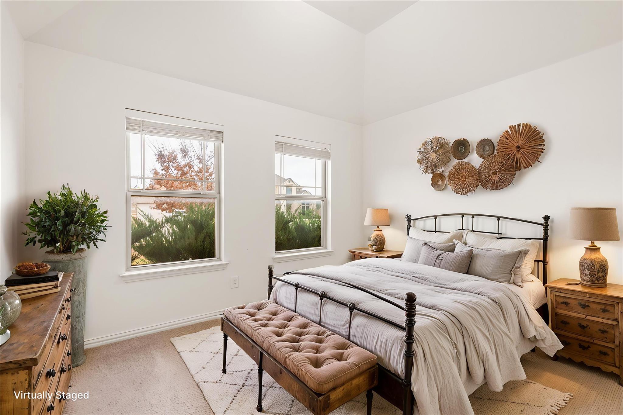 Virtually staged bedroom with a black metal bed, tufted bench, and two windows beneath a vaulted ceiling.
