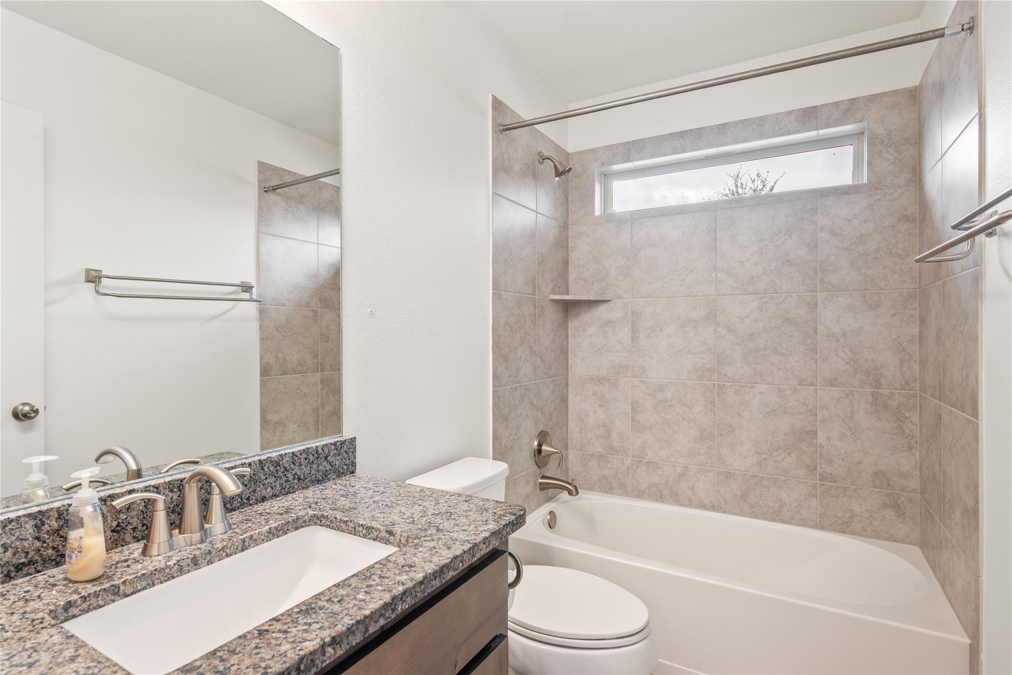 Bathroom with granite vanity and tiled tub-shower surround beneath a high window.