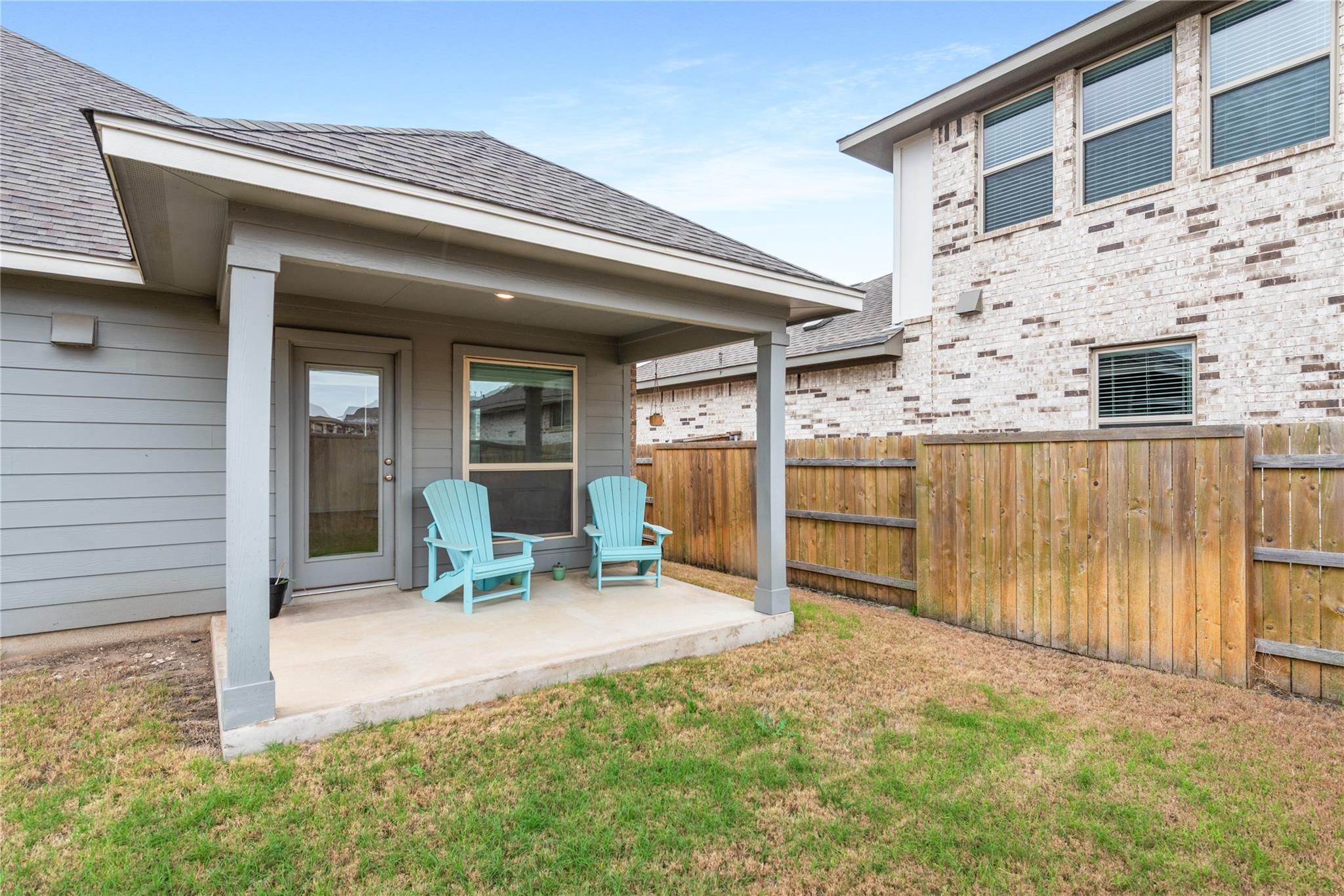 Covered backyard patio with two turquoise Adirondack chairs and a wooden privacy fence.