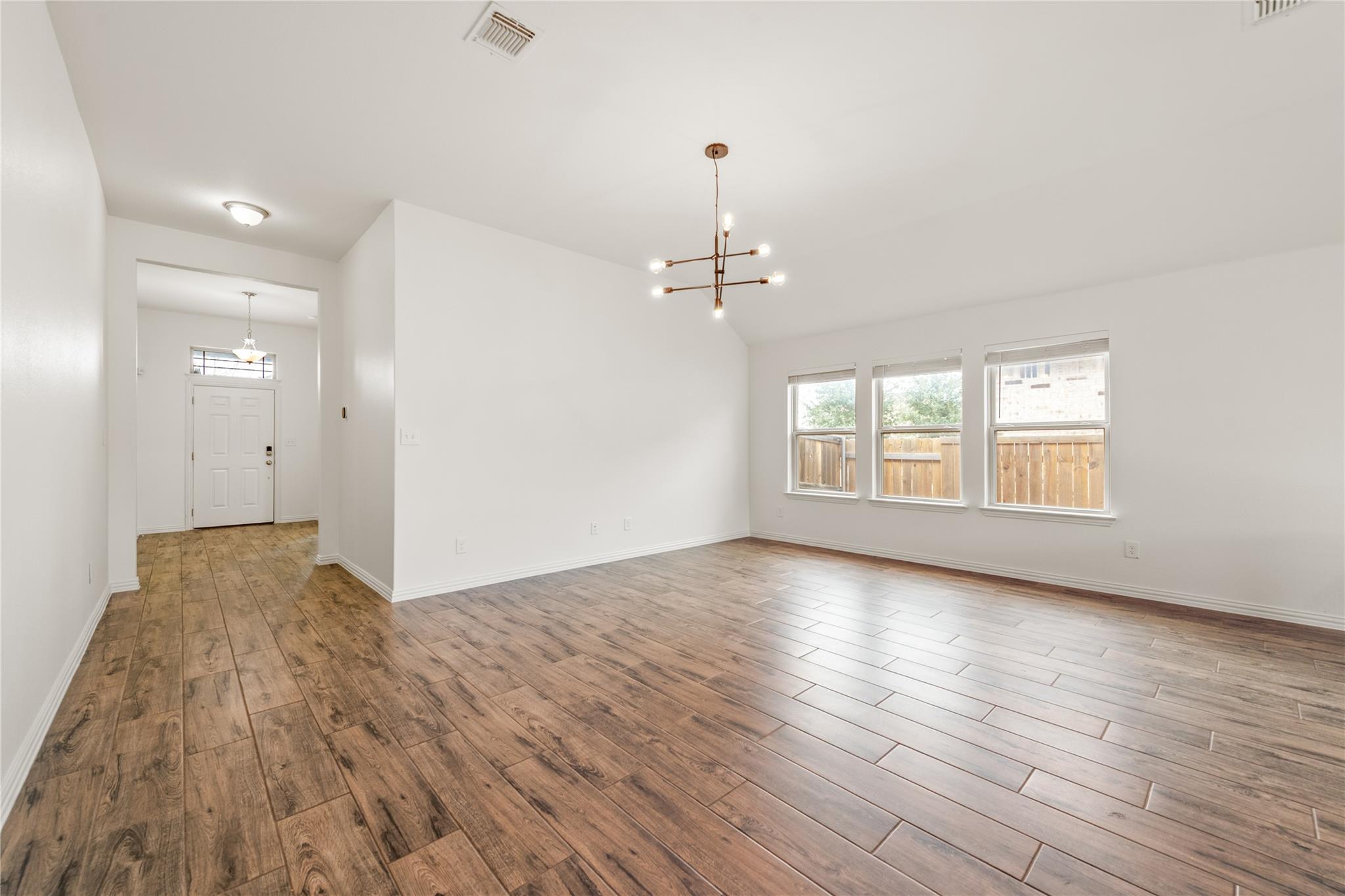 Empty living area with wood-look tile floors, a modern chandelier, and three windows.