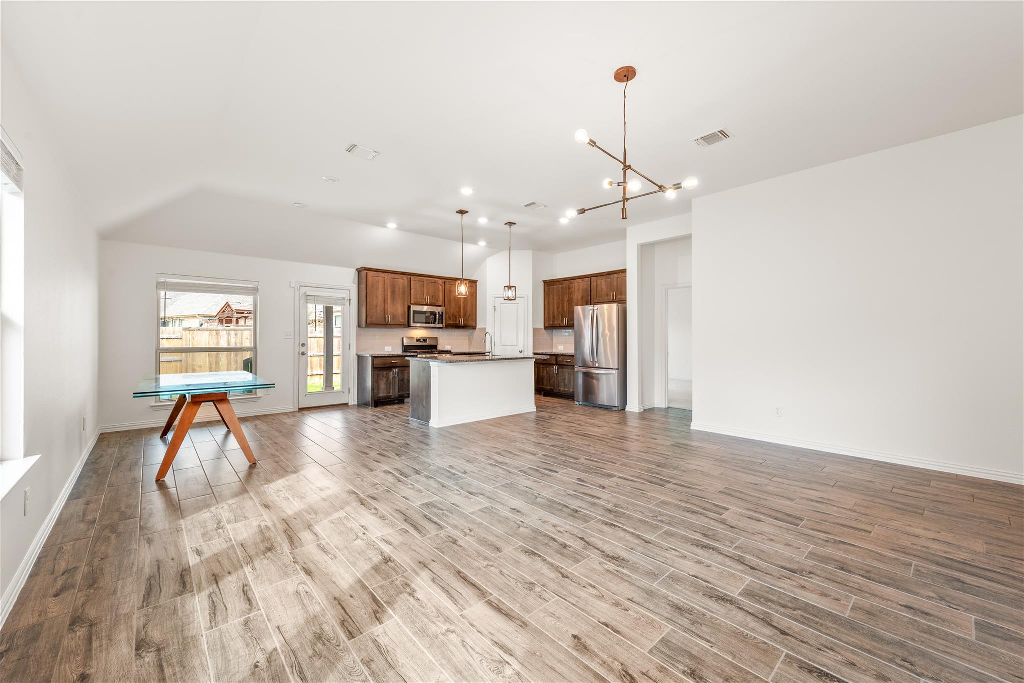Open-plan kitchen and dining area with dark wood cabinets, stainless steel appliances, and wood-look tile floors.