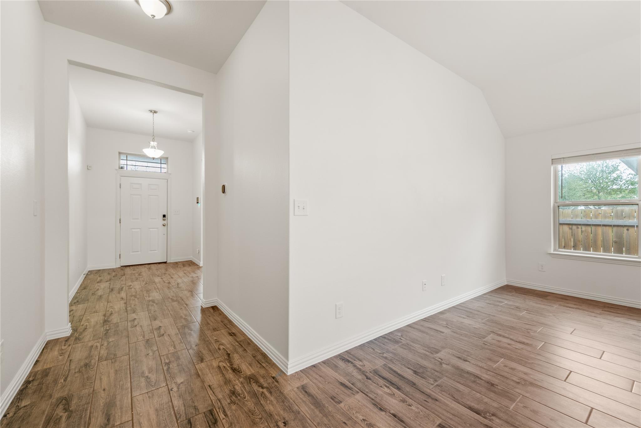 Empty room with wood-look tile floors and a window facing the fenced yard.