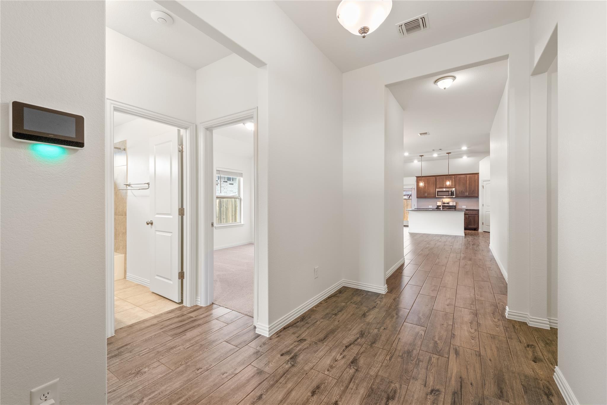 Hallway with wood-look tile floors leading to a kitchen with dark cabinets and a white island.