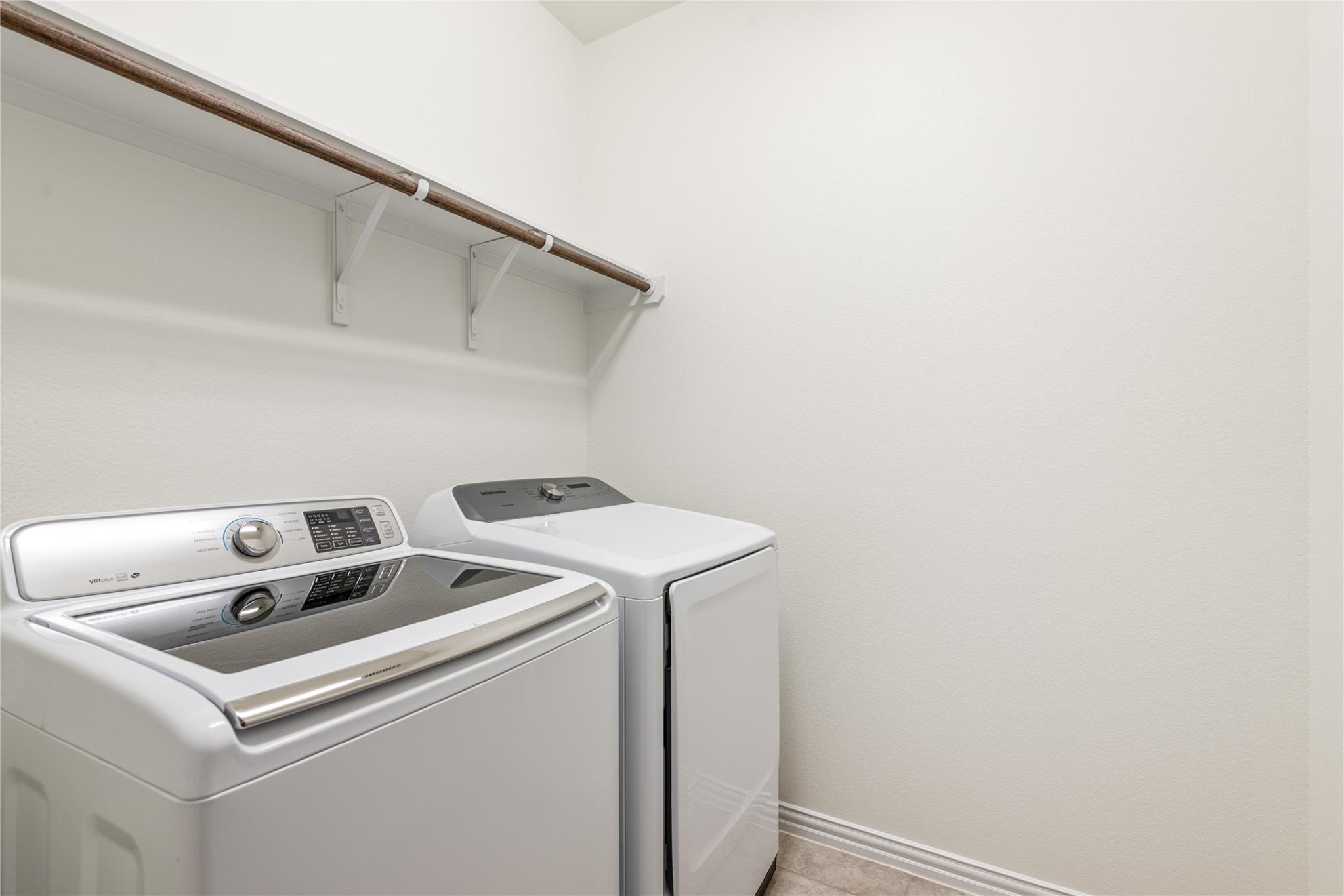 Laundry room with a white washer and dryer beneath a wooden hanging rod.