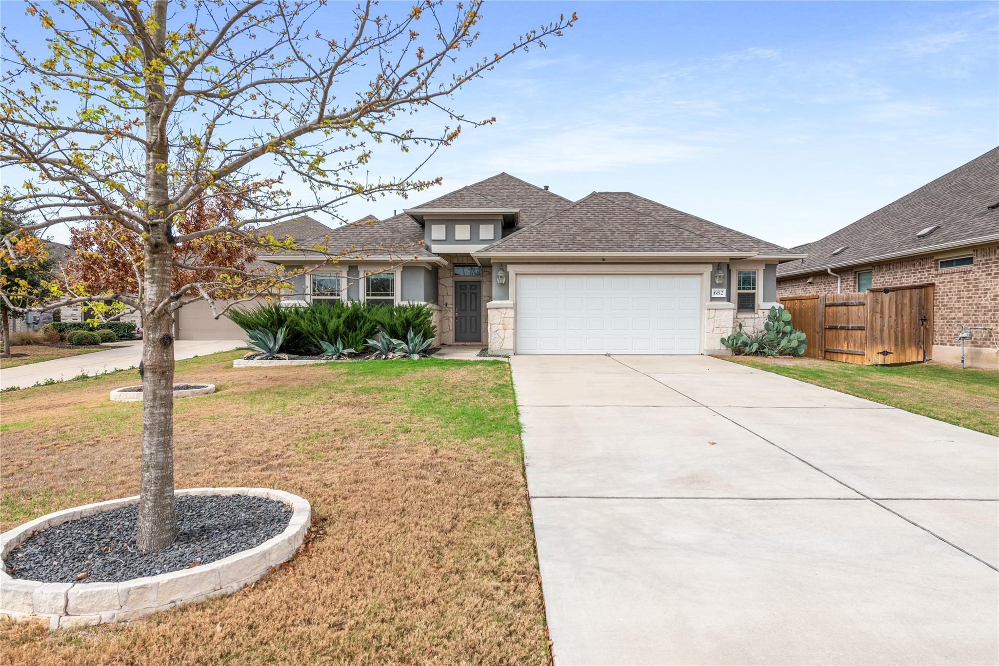 Single-story house with stone accents, a double garage, wide driveway, and a tree in the front yard.
