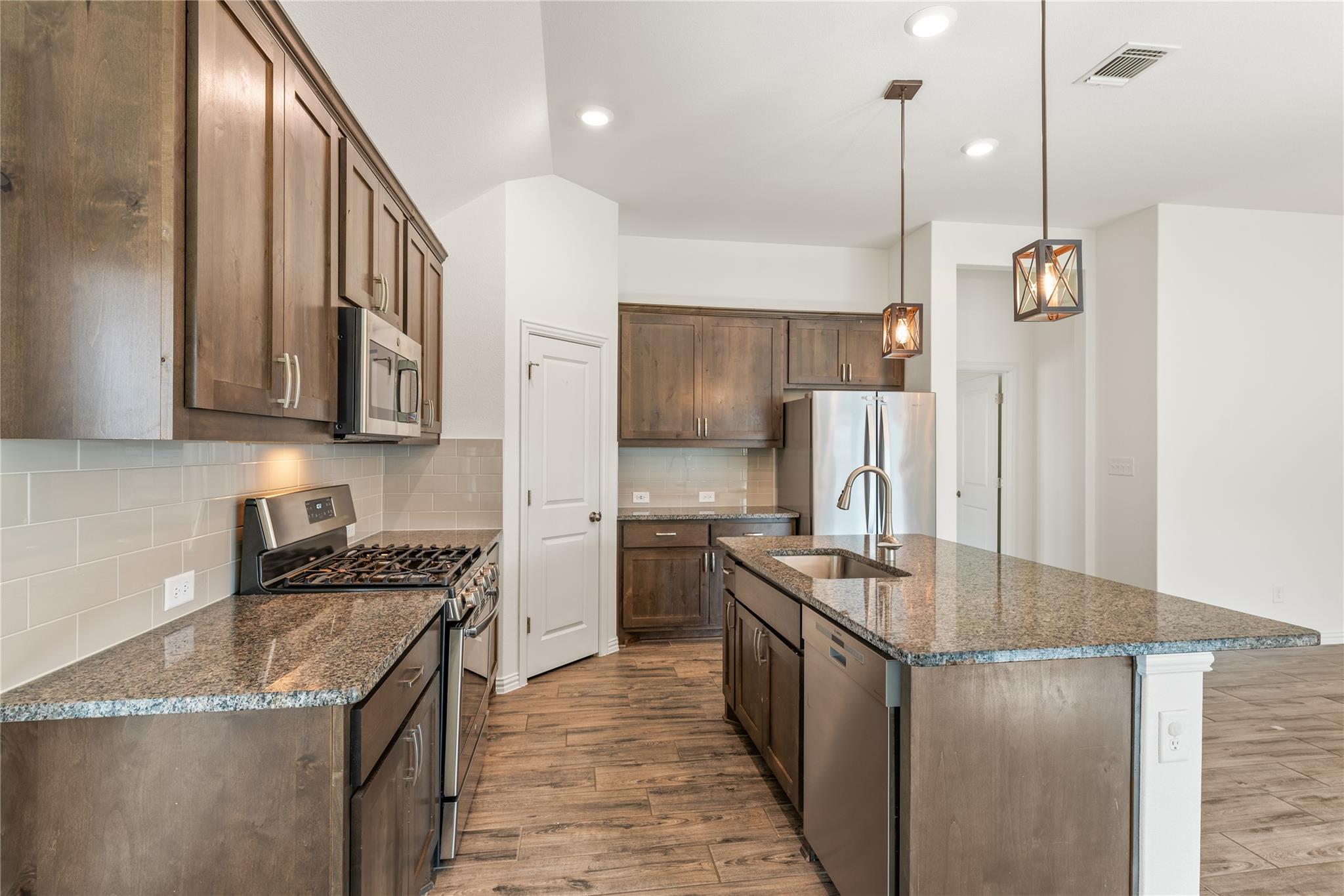 Kitchen with dark wood cabinets, granite island and countertops, stainless steel appliances, and a gas range.