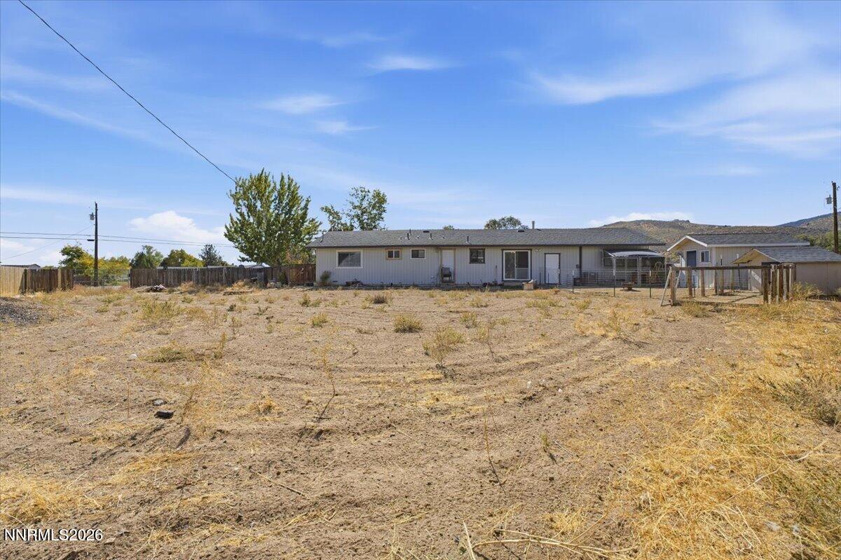 Single-story home beyond a dry fenced yard, with a covered patio and swing set.