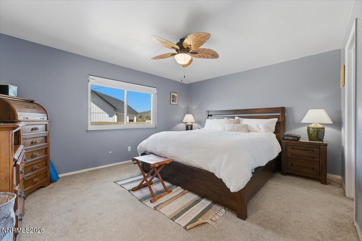 Furnished bedroom with a large white-covered bed, gray walls, and a wood leaf-blade ceiling fan.