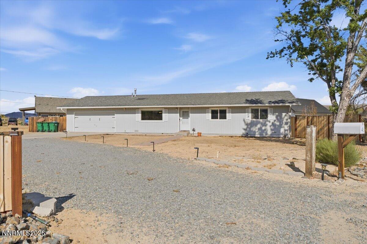Single-story home with an attached garage, broad gravel driveway, and fenced yard.