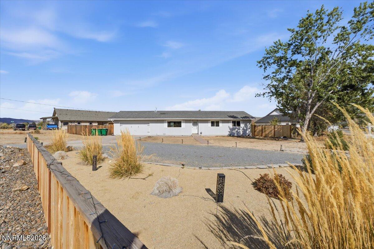 Single-story home with a gravel driveway, xeriscaped yard, wooden fence, and large tree.