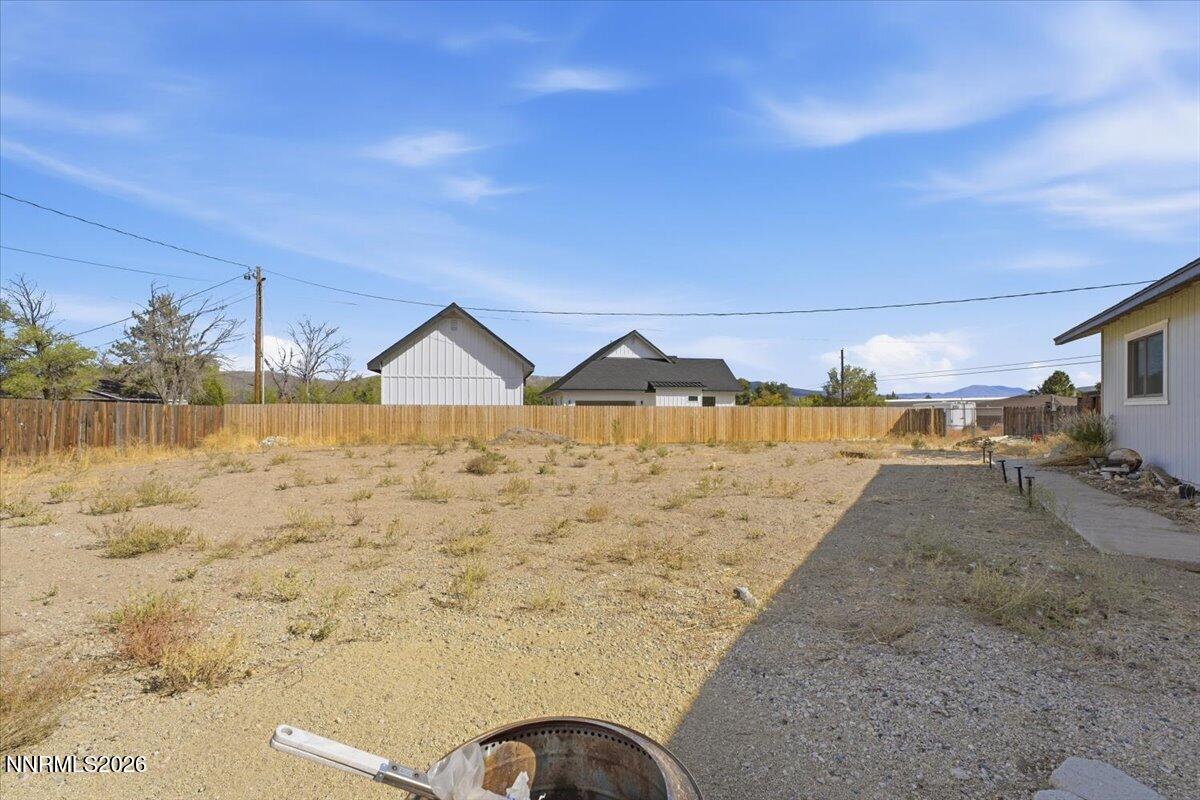 Mostly bare gravel backyard with a wooden fence, neighboring buildings, and distant mountains.