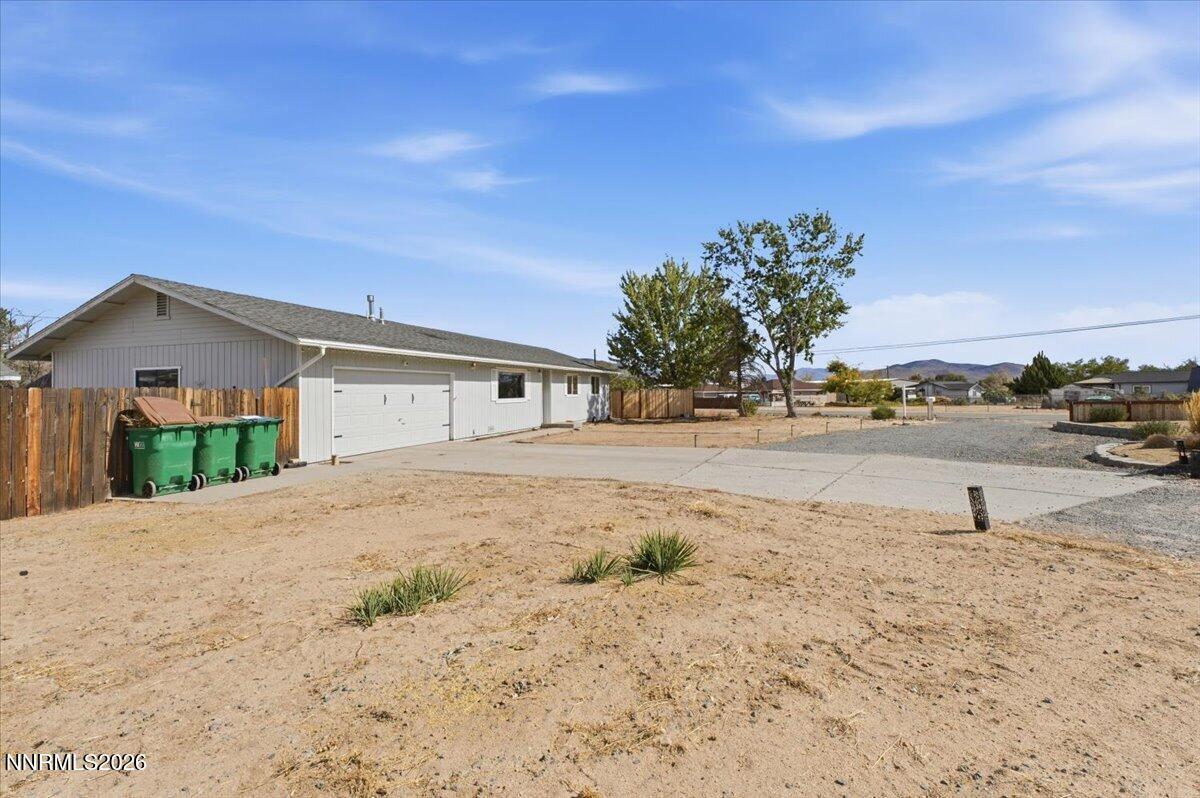 Single-story home with an attached garage, broad driveway, wooden fencing, and dry yard.