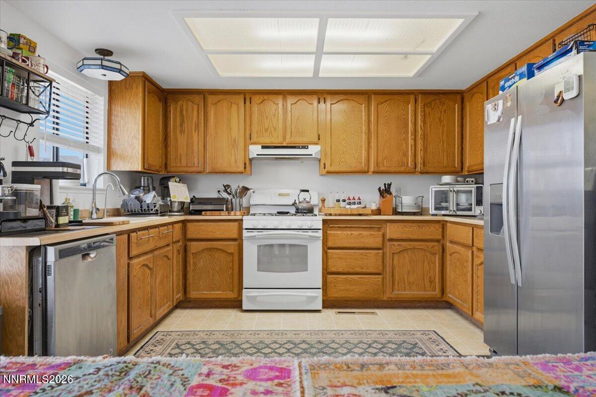 Kitchen with honey-colored oak cabinets, white range, stainless appliances, and a patterned rug.