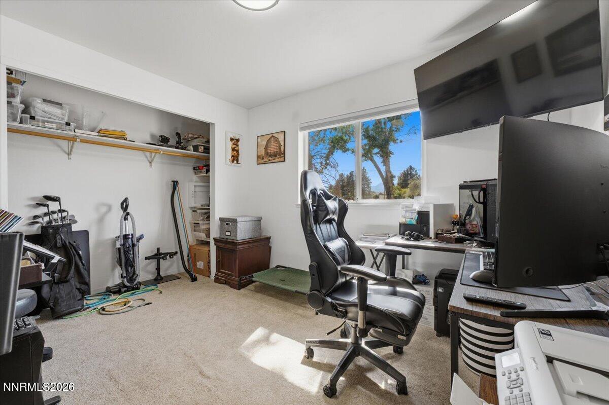 Furnished home office with open shelves, a black gaming chair, and a window overlooking trees.