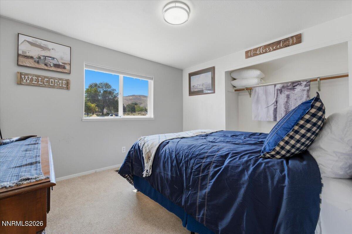 Bedroom with a blue quilted bed, open closet, and window overlooking a hillside.
