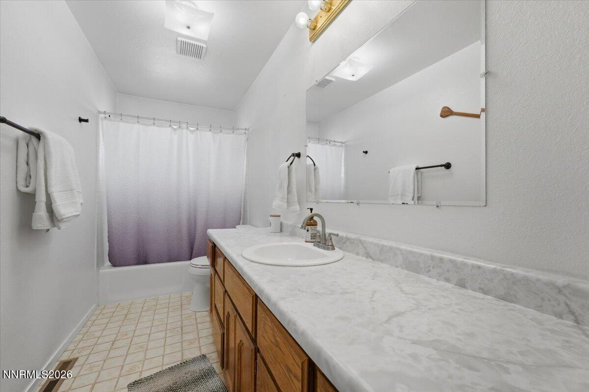 Bathroom with a long marble-look vanity, wood cabinets, and a tub behind a gradient shower curtain.
