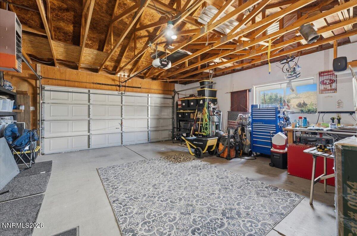 Garage with exposed roof framing, a large patterned rug, storage bins, and workshop equipment.