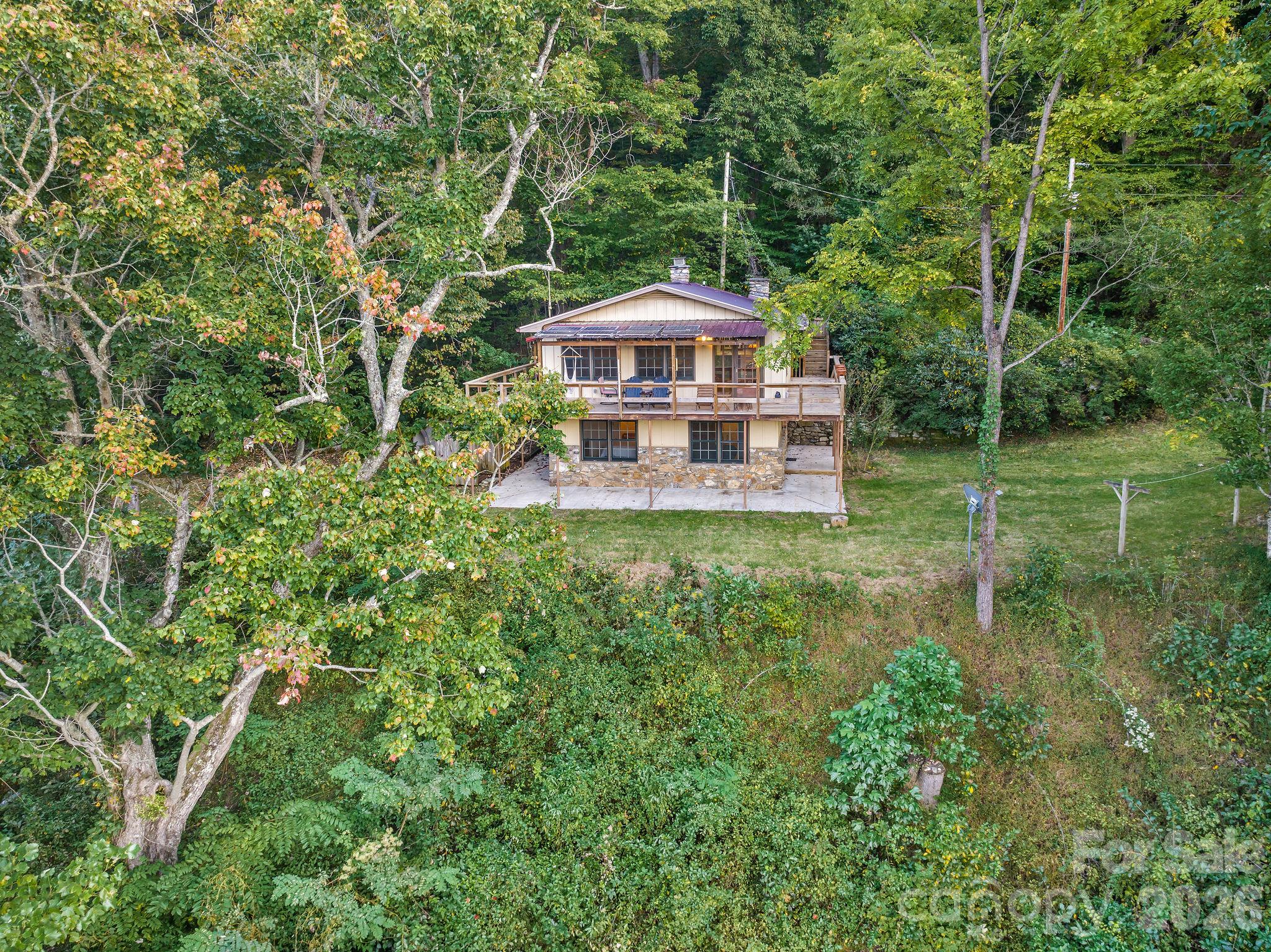 Two-story house with a covered porch and stone foundation in a wooded clearing.
