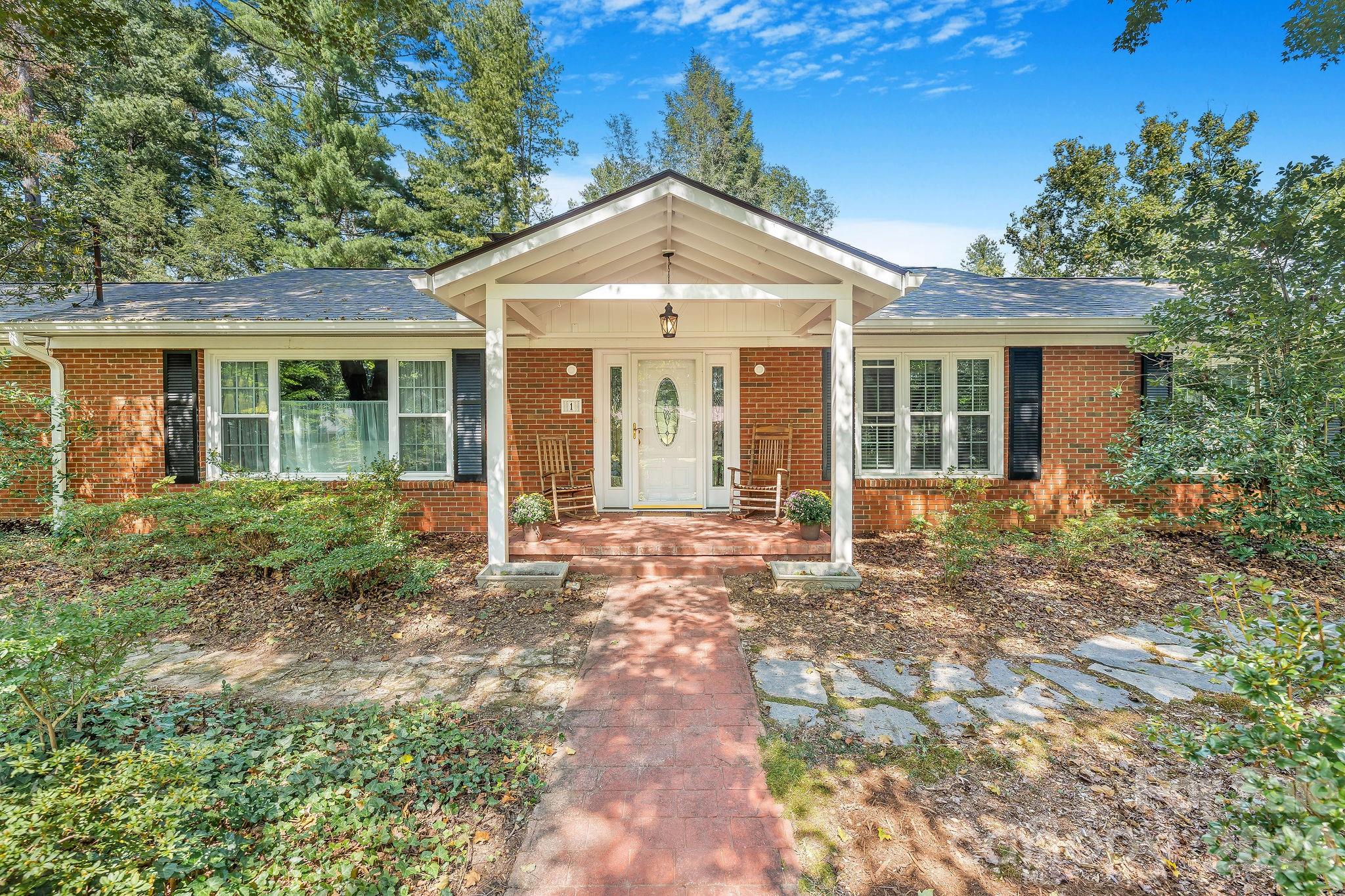 Single-story brick home with a white covered entry, rocking chairs, and a brick walkway.