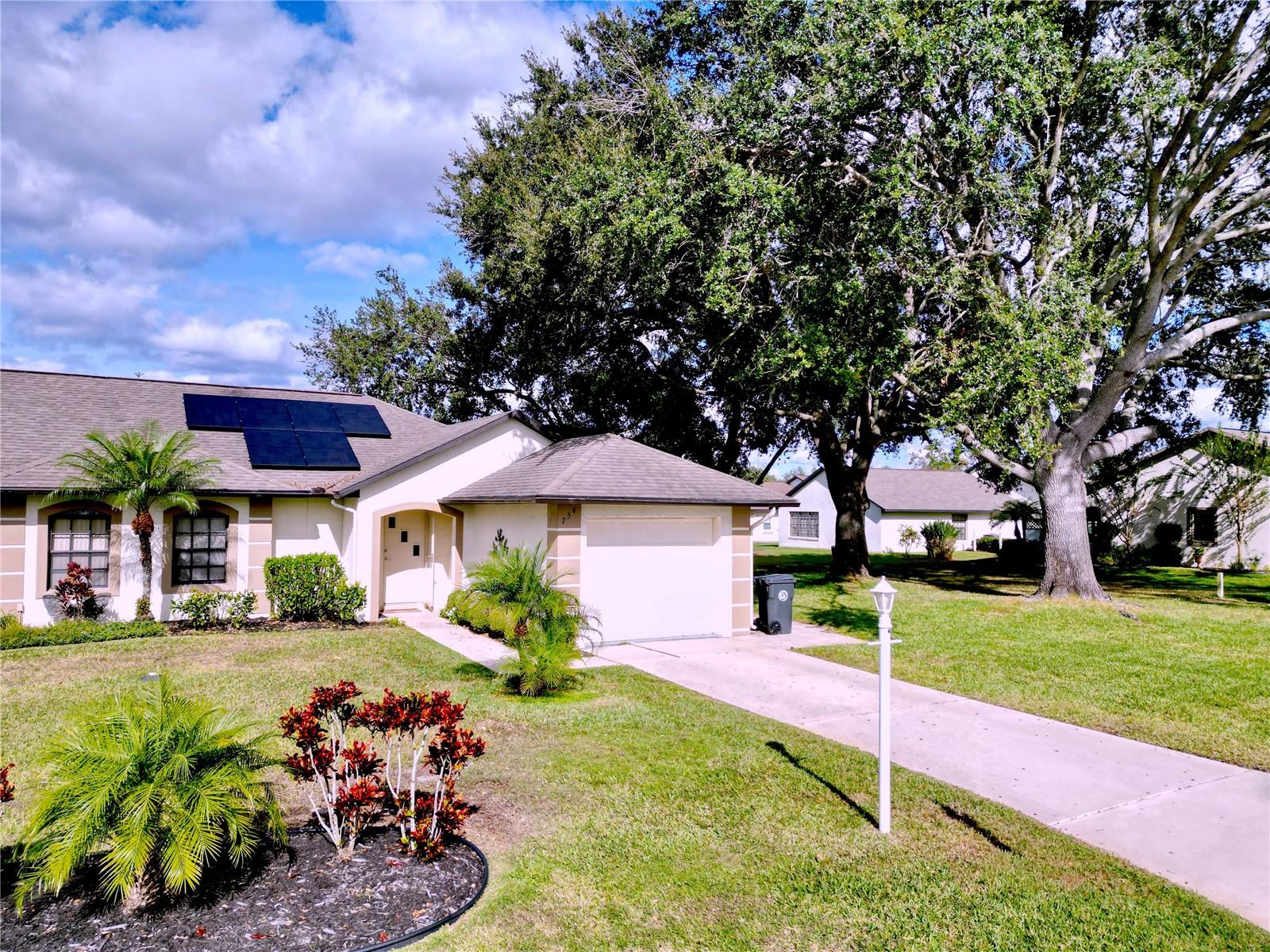 Single-story home with rooftop solar panels, an attached garage, landscaped lawn, and mature shade trees.