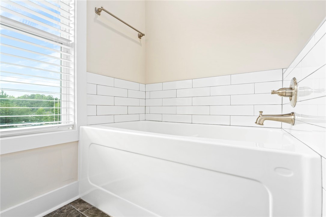 Bathroom with a white bathtub, subway tile surround, and a window with blinds.