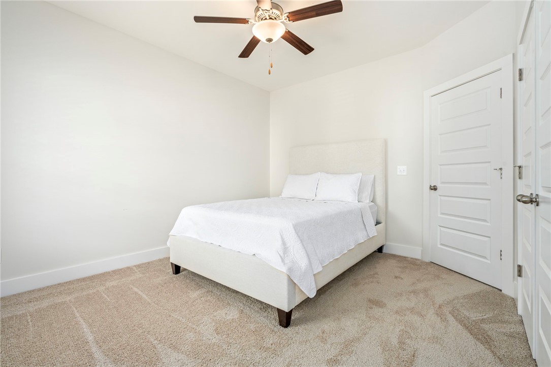 Bedroom with a white bed, beige carpet, paneled doors, and a dark-bladed ceiling fan.