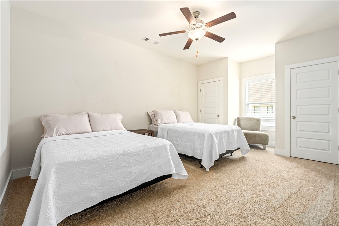 Bedroom with two white-covered beds, beige carpet, and a ceiling fan.