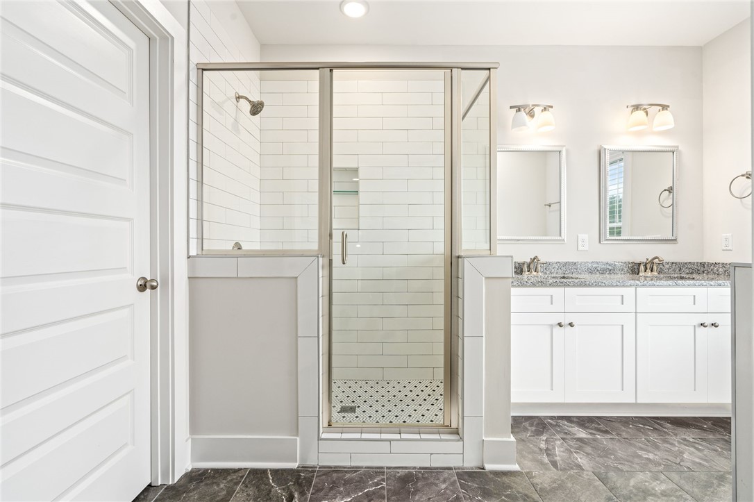 Bathroom with a glass-enclosed subway-tile shower and double-sink vanity.