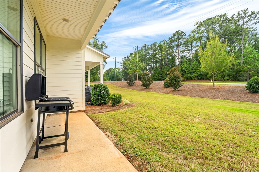 Covered patio with a black grill overlooking a lawn and tree-lined yard.