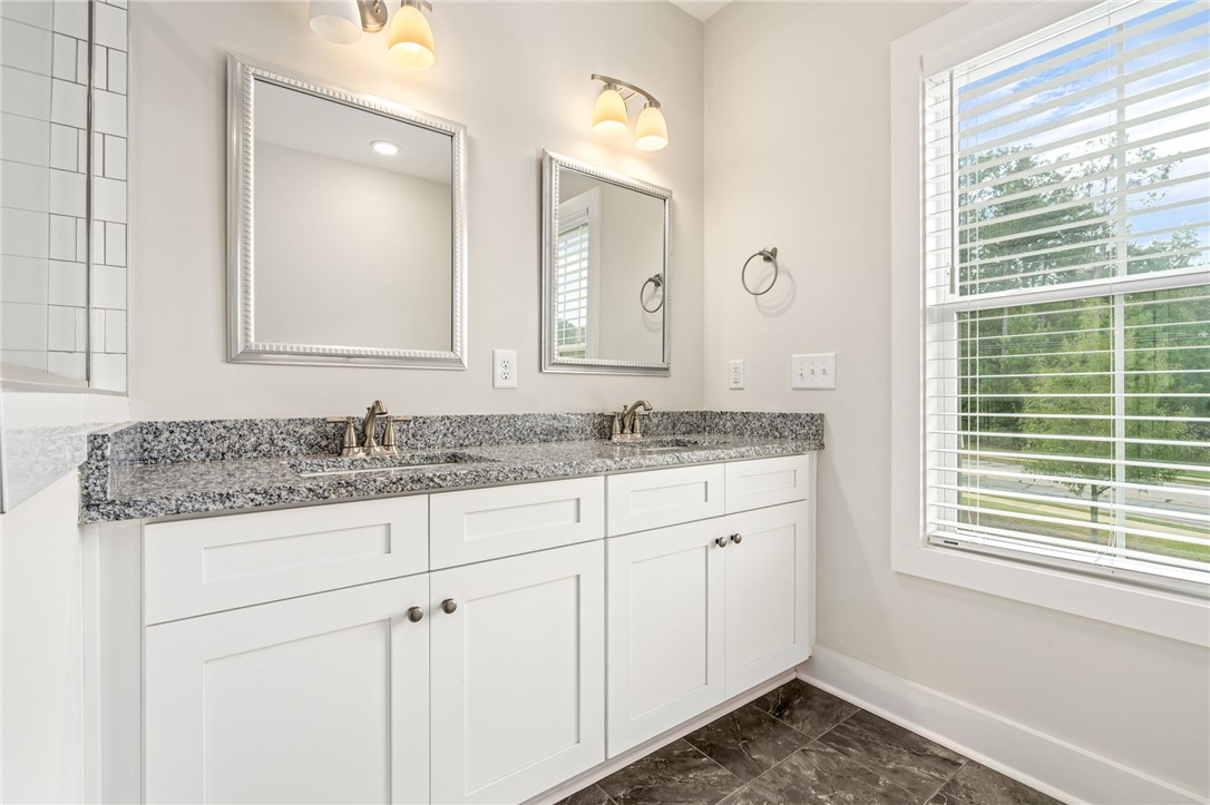 Bathroom with a white double vanity, granite countertop, paired mirrors, and a large window with blinds.