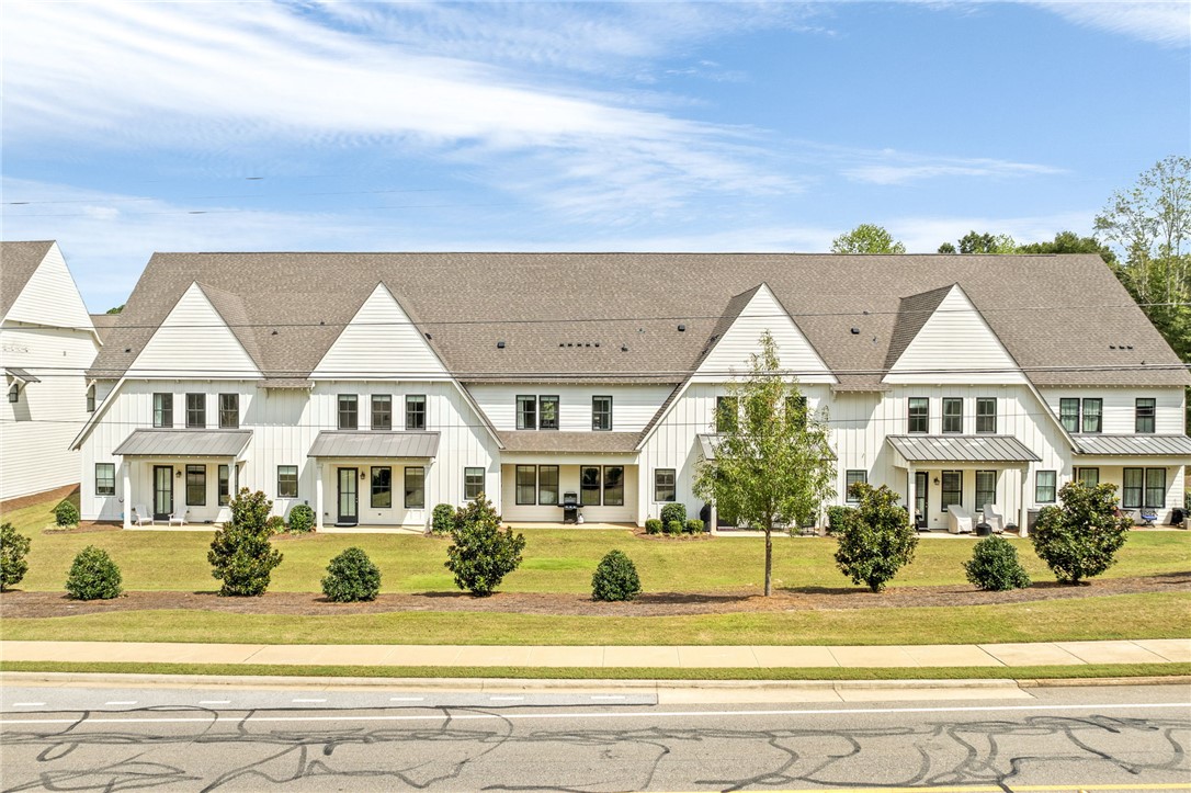 White attached townhomes with steep gabled roofs, front porches, and landscaped lawn.