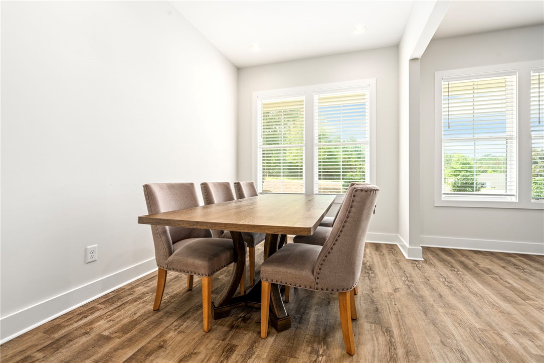 Dining room with a wooden table, upholstered chairs, and large windows with white blinds.
