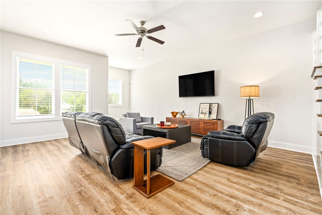 Furnished living room with black leather seating, large windows, and a wall-mounted television.