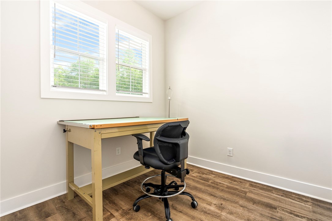 Home office with a drafting table and black chair beneath two windows.