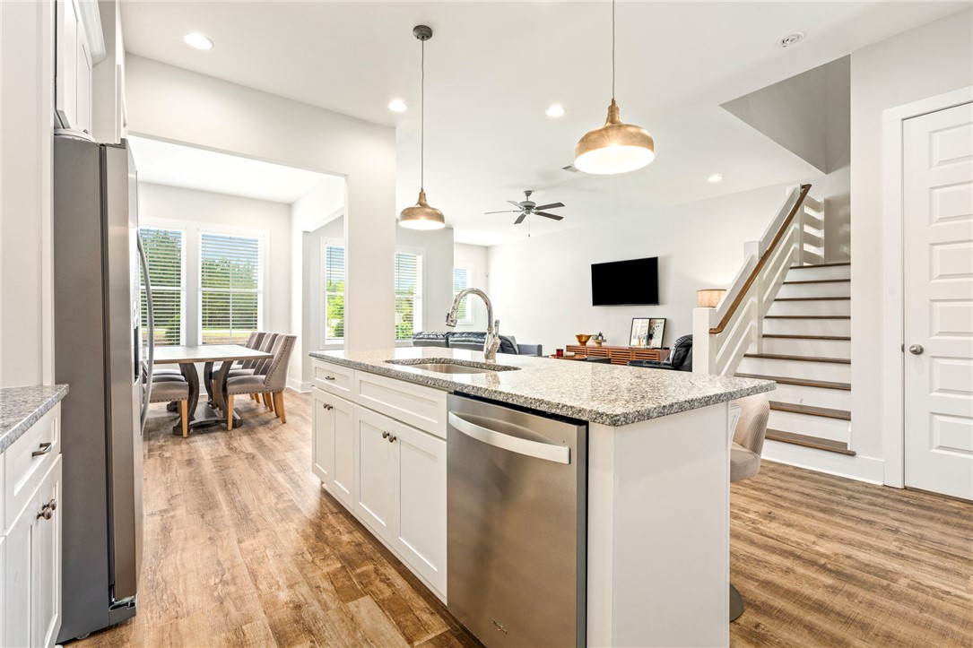 Open-plan kitchen with a granite island, stainless steel dishwasher, dining area, and staircase.