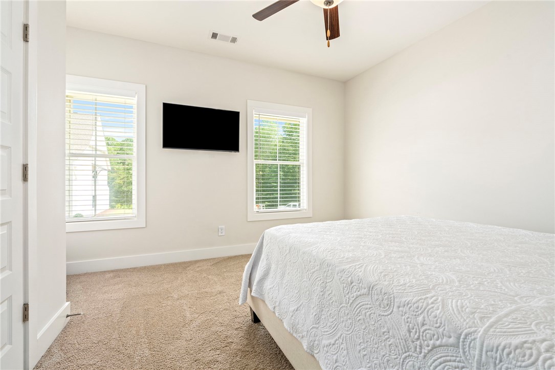 Bedroom with a white quilted bed, two windows with blinds, and a wall-mounted television.