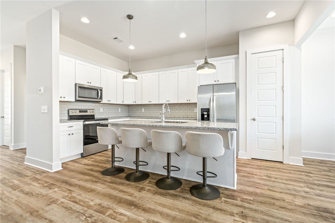 Bright kitchen with white cabinets, stainless steel appliances, and a four-seat island.