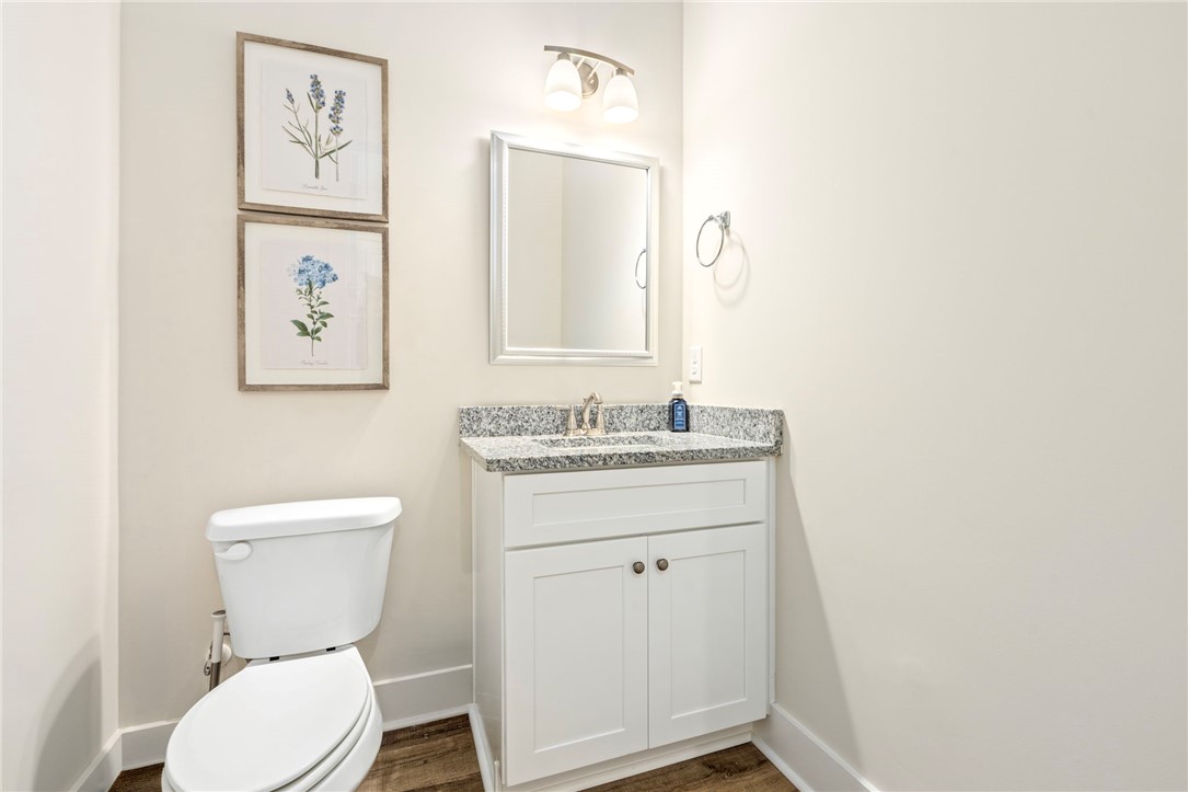Bathroom with a white vanity, speckled granite countertop, toilet, and framed botanical prints.