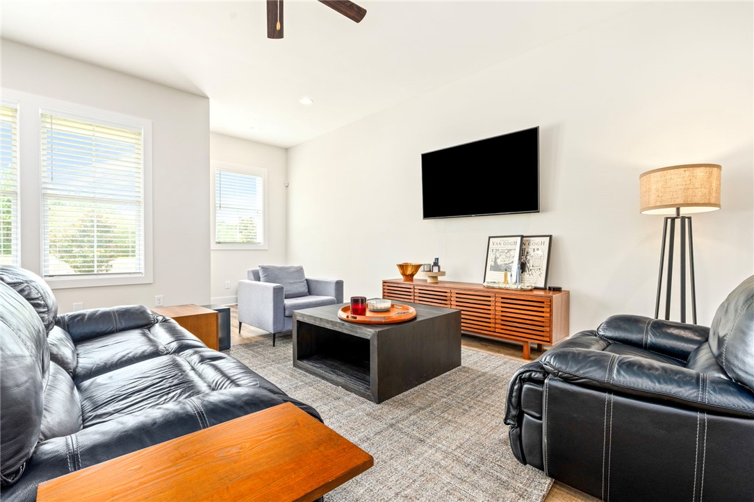 Living room with black leather sofas, a gray armchair, and a wood media console beneath a wall-mounted TV.