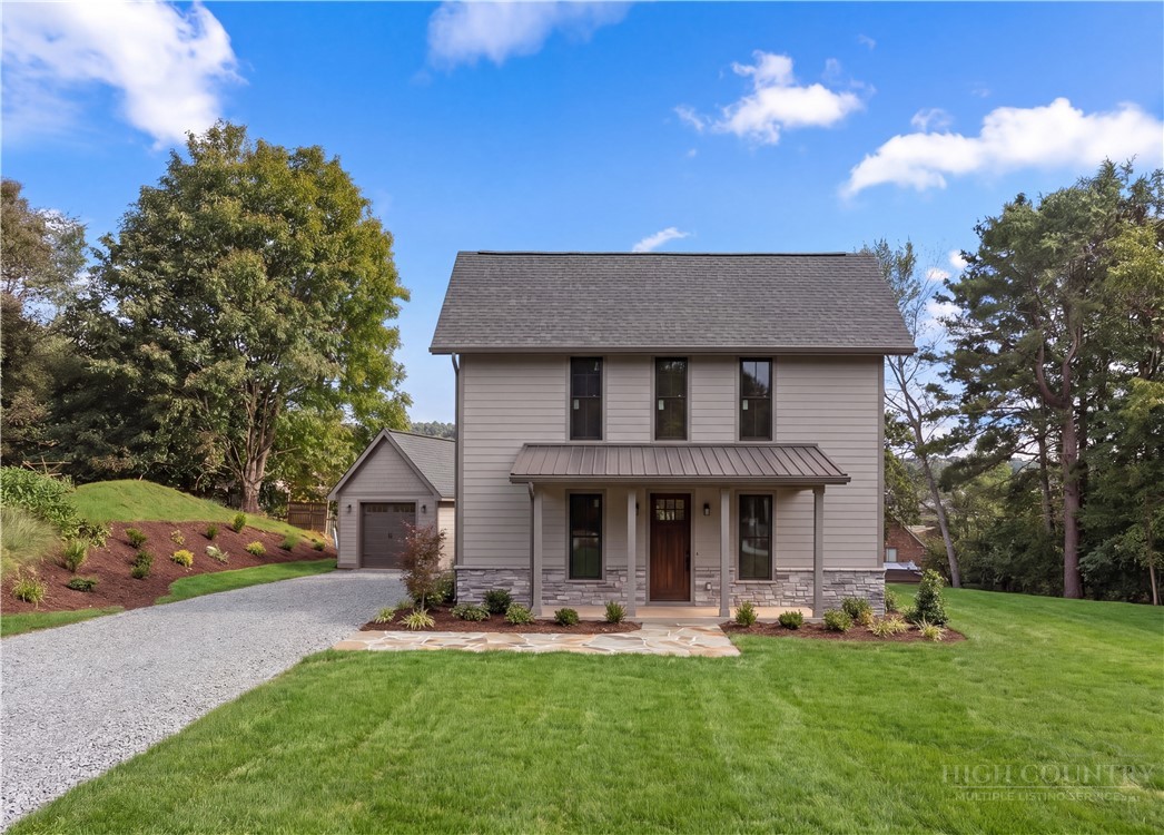 Two-story gray home with a covered porch, stone accents, detached garage, and landscaped lawn.