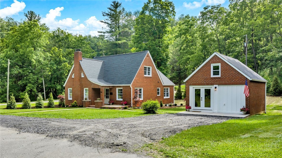 Red brick house and detached garage beside a gravel driveway, surrounded by green lawn and mature trees.