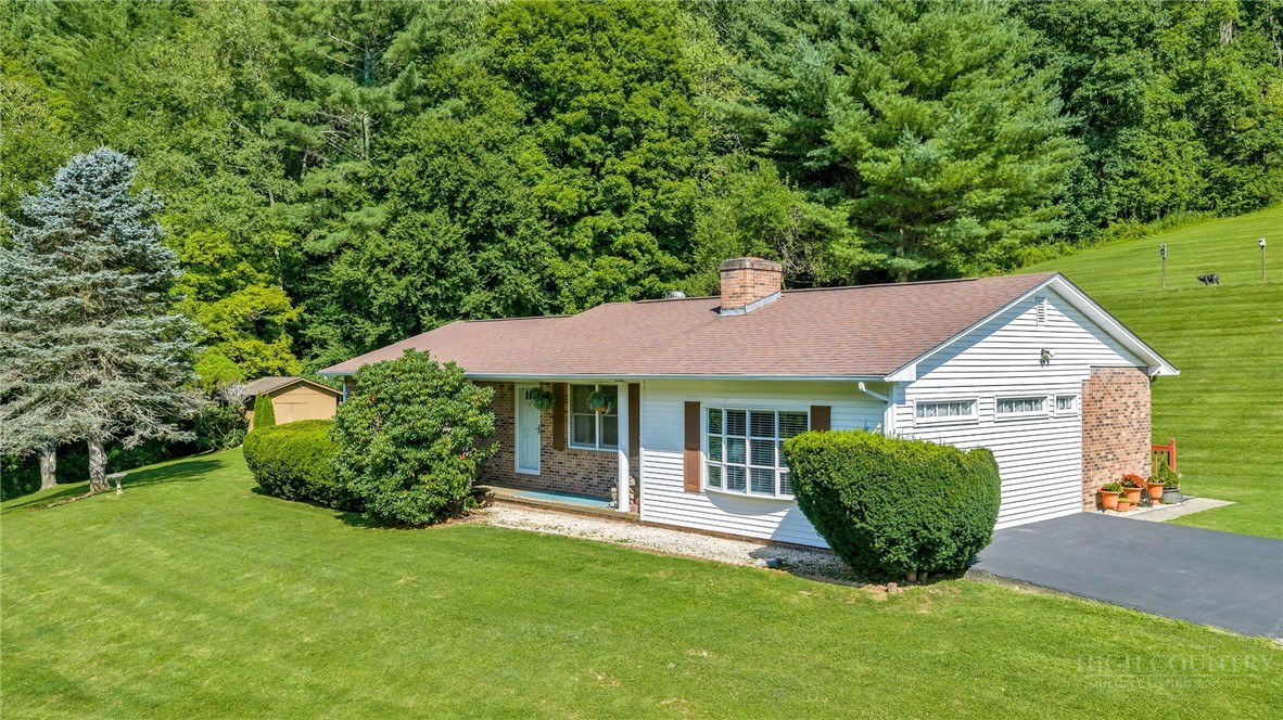 Single-story ranch home with white siding, brick accents, and a wooded backdrop.