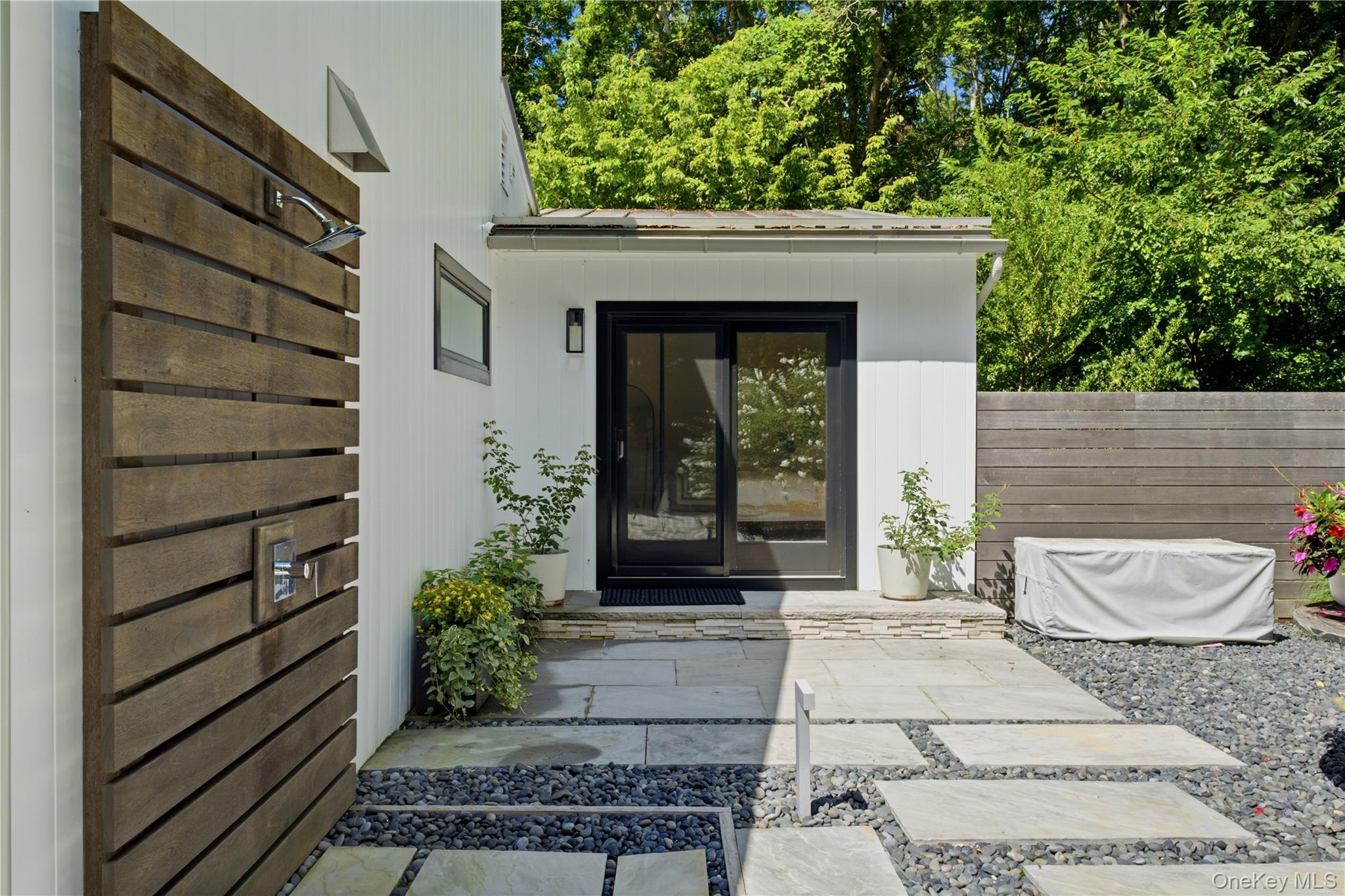Modern home patio with a wood-slat outdoor shower screen and black-framed sliding glass doors.