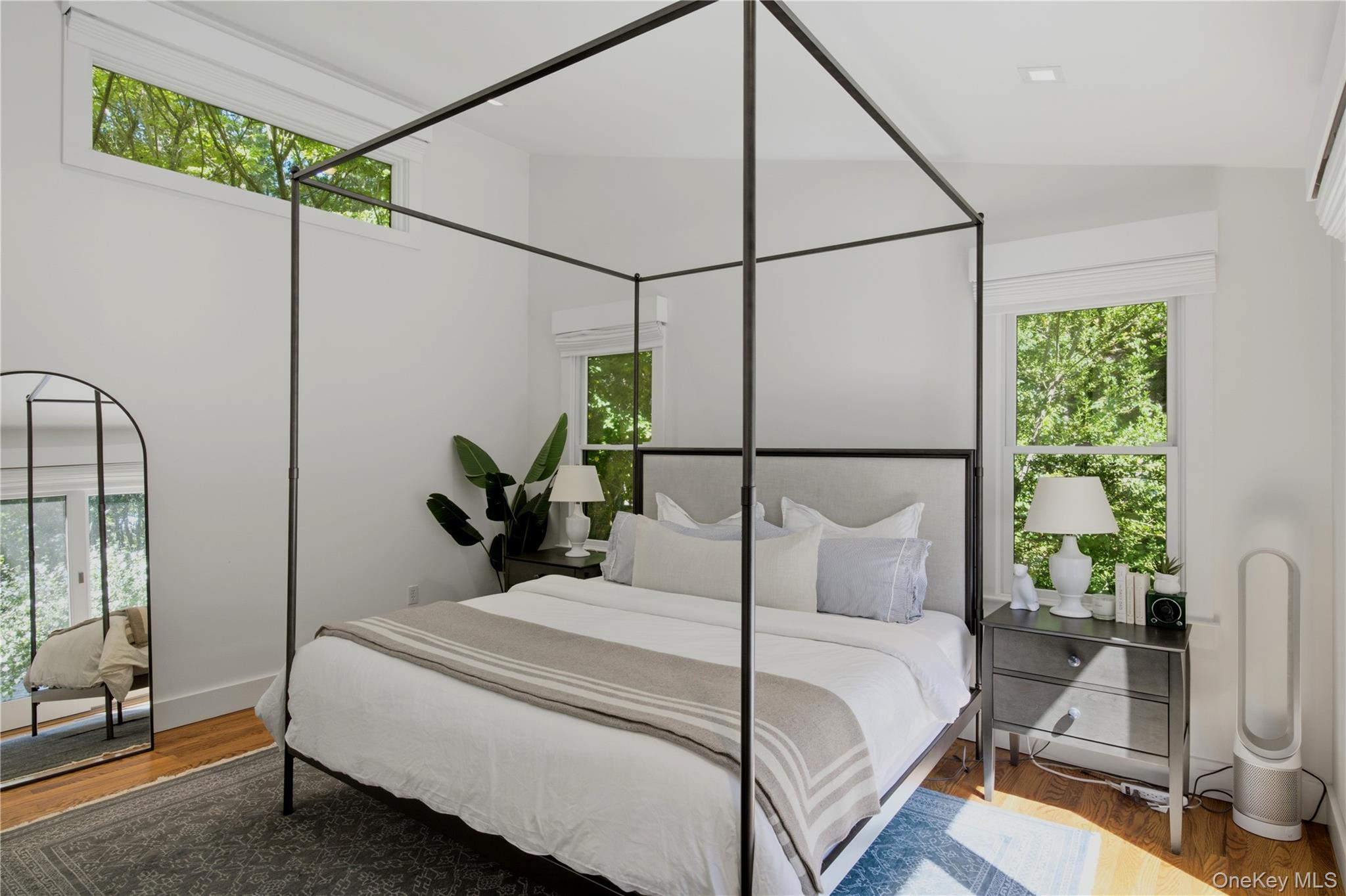 Bright bedroom with a black canopy bed, wood floors, and windows overlooking leafy trees.