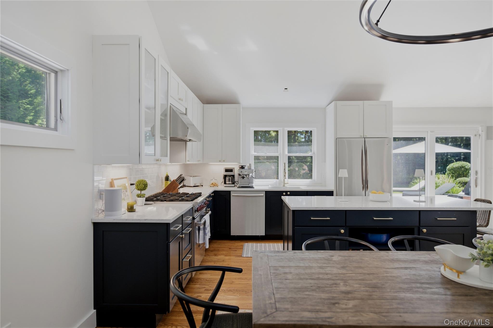Modern kitchen with a large island, dark cabinetry, stainless steel appliances, and windows overlooking greenery.